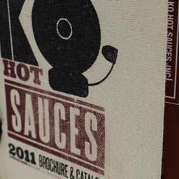 Photo of deluxe trade show brochure for KO Hot Sauces, showing off the canvas cover, screen printing and laced binding.